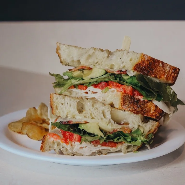 Stacked gourmet sandwich on artisan bread with chips at Niko's Bakery & Cafe
